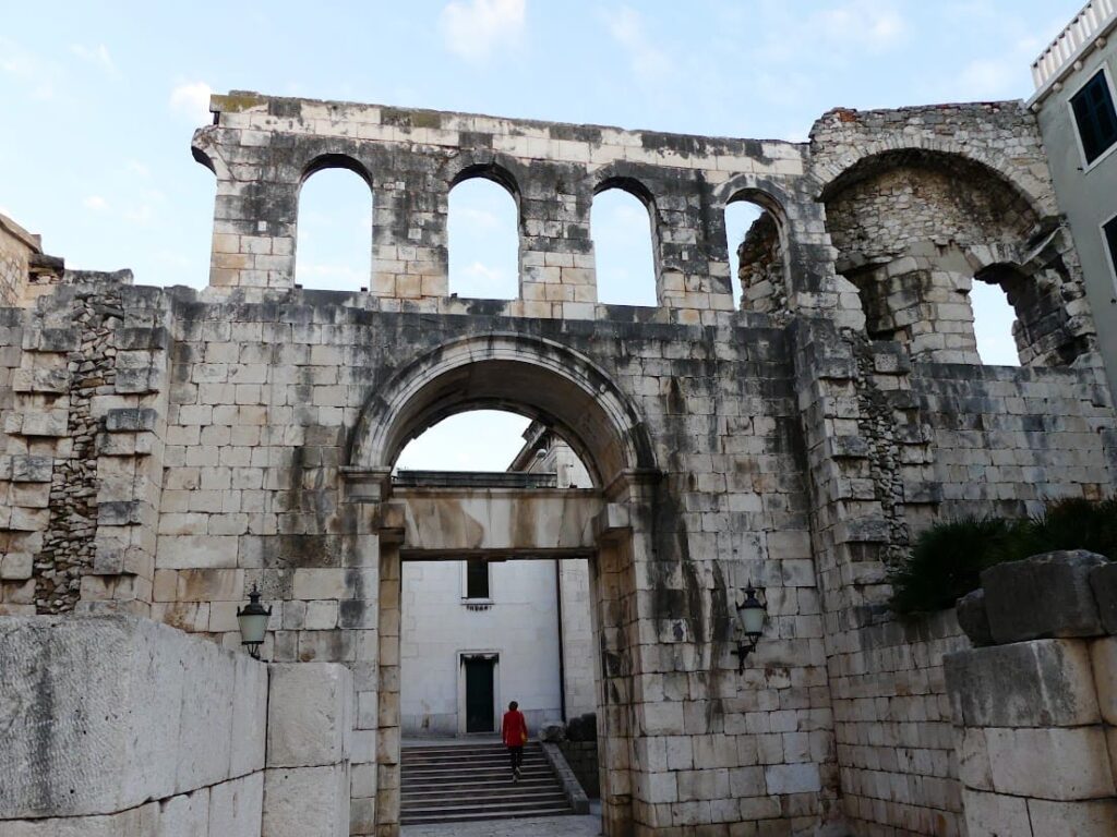 The walls of the old town in Split, Croatia, with a lady in a red coat walking through the ancient archway.